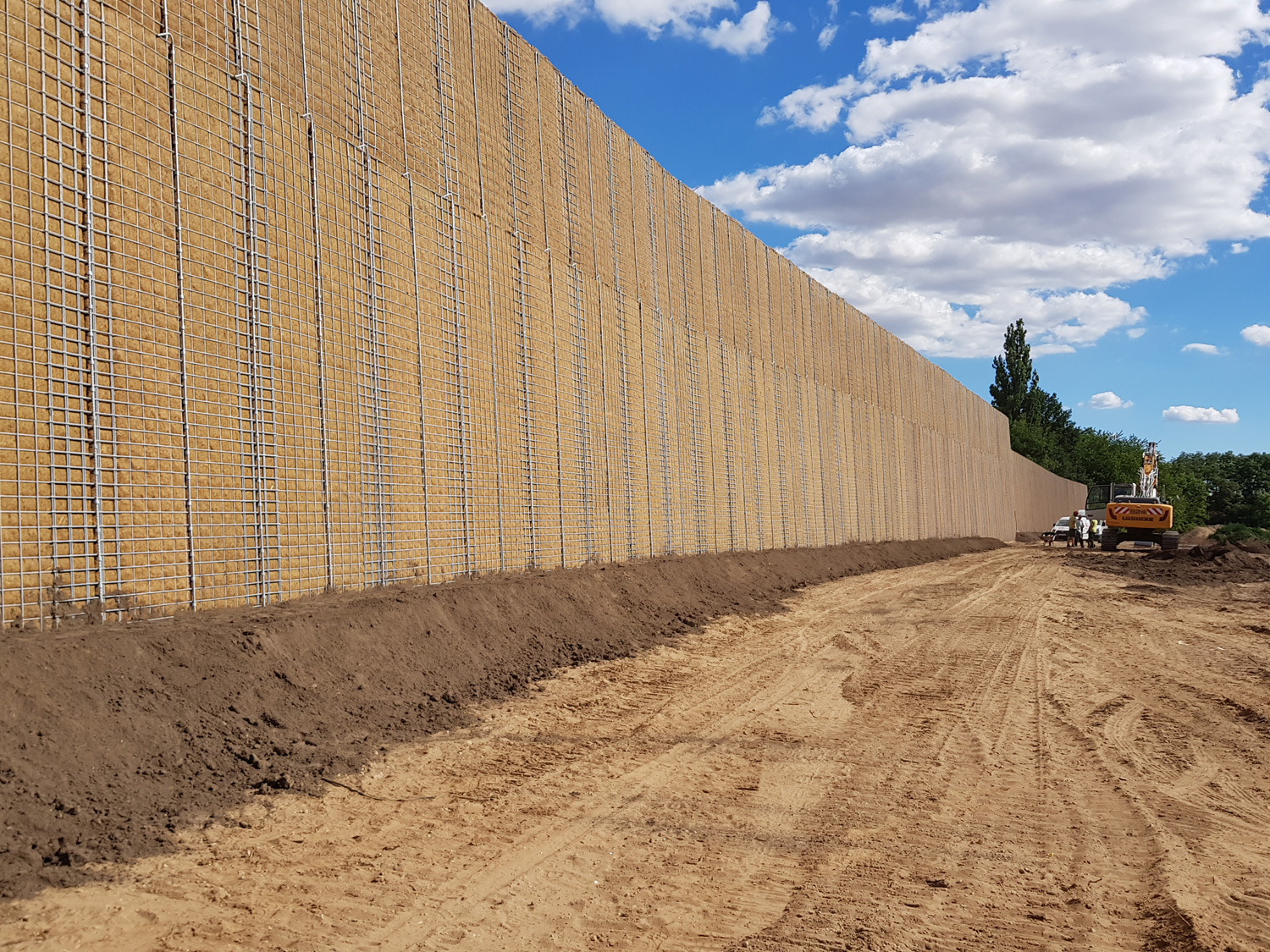 Noise barrier with trellises next to a construction site.