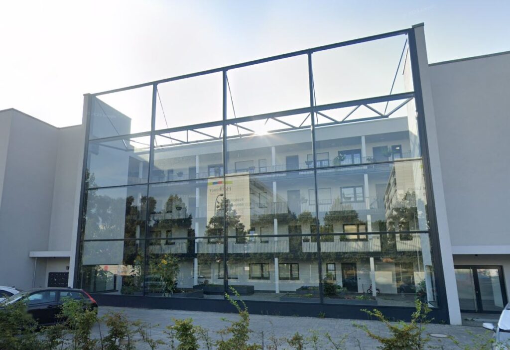 Mur anti-bruit en verre entre deux bâtiments, soutenu par un cadre en acier et offrant une vue sur la cour intérieure située derrière.