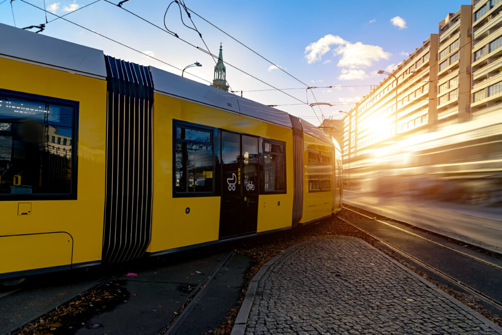 Gelbe Straßenbahn fährt durch die Stadt bei tief stehender Sonne, mit Bewegungsunschärfe