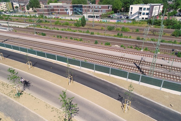Luftaufnahme einer Bahnstrecke mit Schallschutzwand und parallel verlaufendem Fuß- und Radweg