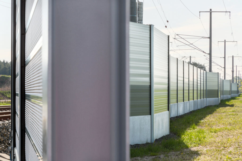 Nahaufnahme einer modernen Schallschutzwand entlang von Bahngleisen mit Oberleitungen