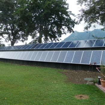 Solaranlage auf einer Lärmschutzwand, umgeben von einer grünen Wiese und Bäumen